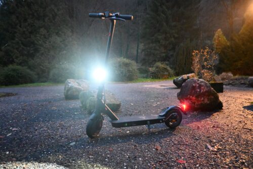 iScooter E9Pro E-Scooter parkt mit leuchtendem Rücklicht in der Abenddämmerung.